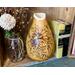 A handmade sunflower vase that is part of an open shelving display. The vase is made from a dried gourd. It sits next to vintage books.